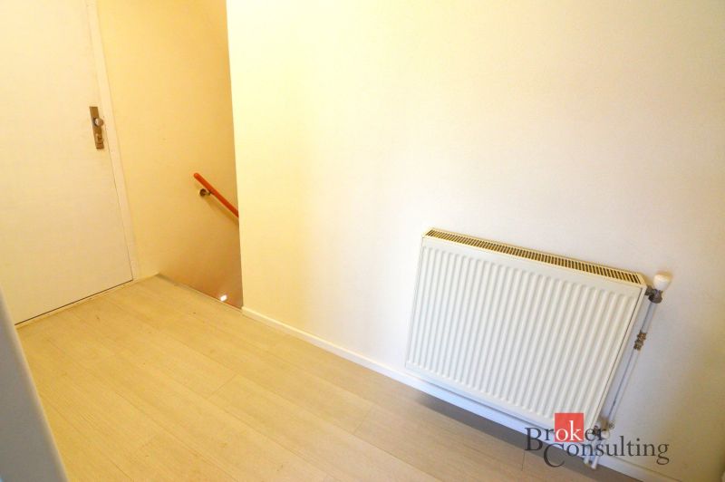 A hallway with a wooden decor floor, a radiator, and a staircase in a 2-room apartment.