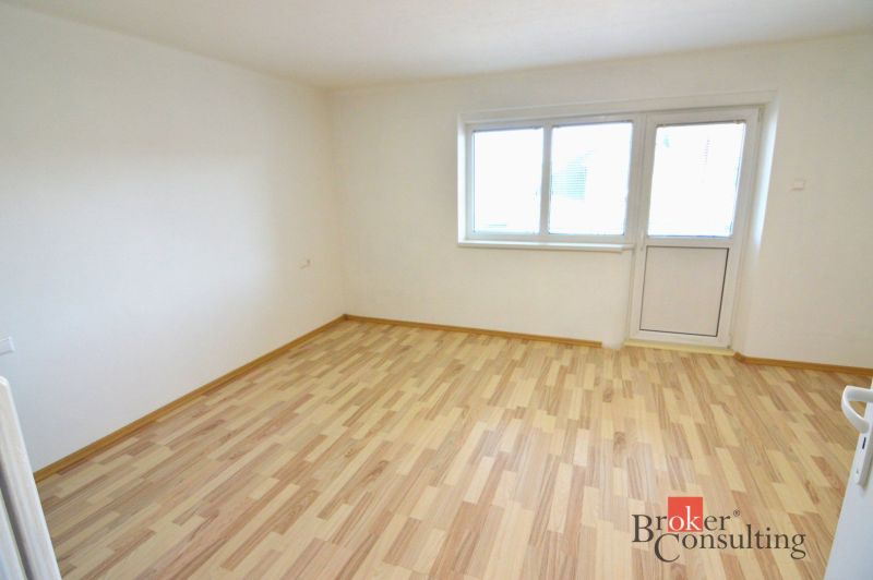 A bright room with wood-decor flooring in a 2-room apartment with access to a balcony.