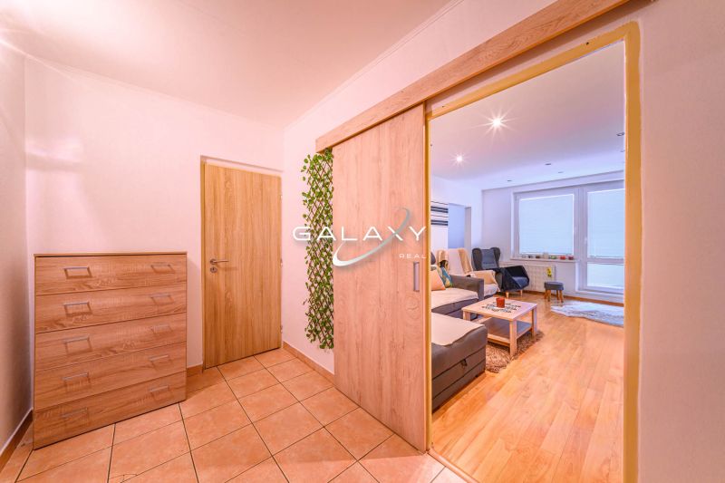 Living room of a two-room apartment with a wooden decor floor and an entrance hall.