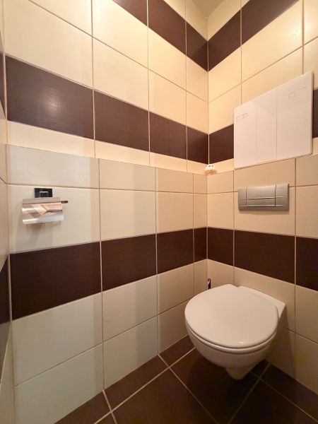 A toilet in a 3-room apartment with brown and white tiles.