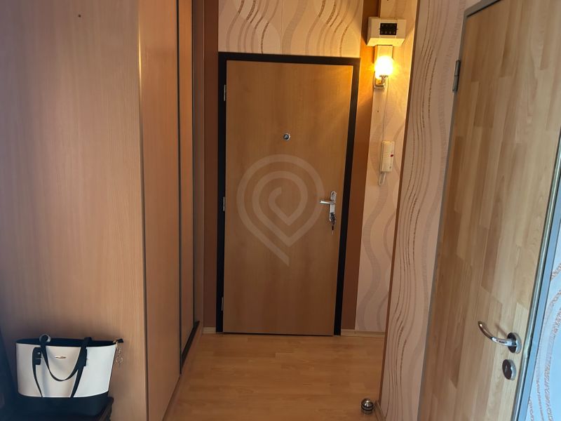 A hallway in a 3-room apartment with a wooden decor floor and a wall lamp.