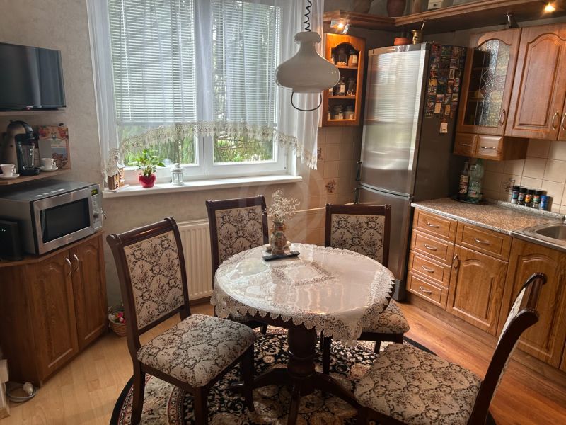 A kitchen in a 3-room apartment with a wooden decor floor and a lace tablecloth on the table.
