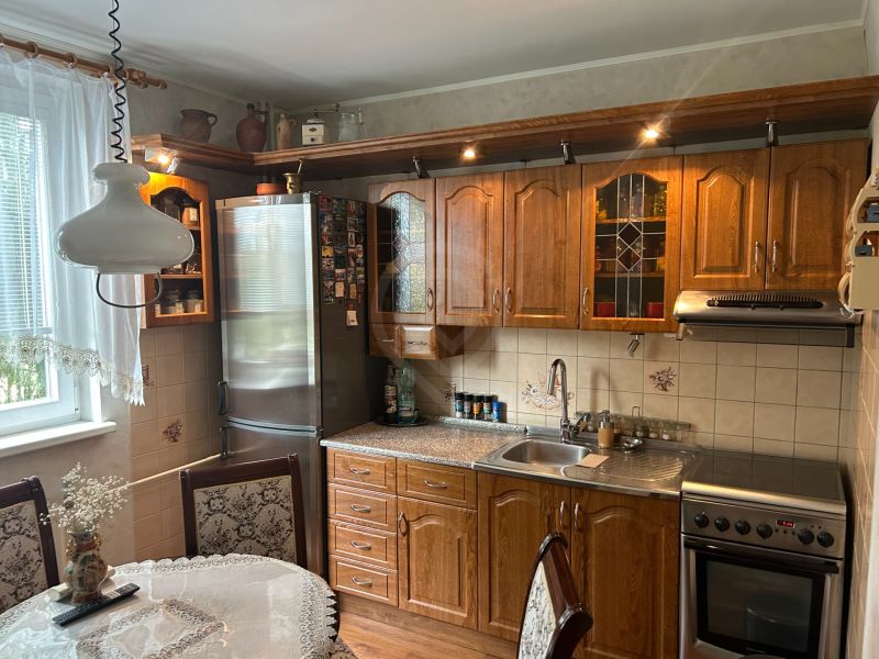 A kitchen in a 3-room apartment with wooden furniture, a decorative curtain, and a dining table.