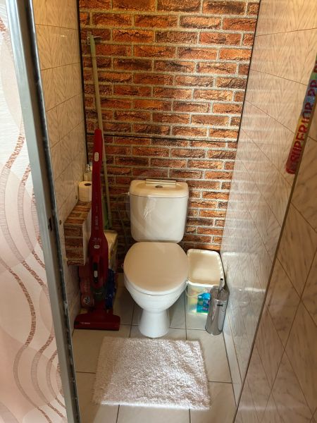 A bathroom in a 3-room apartment with a toilet, brick pattern, and cleaning products.