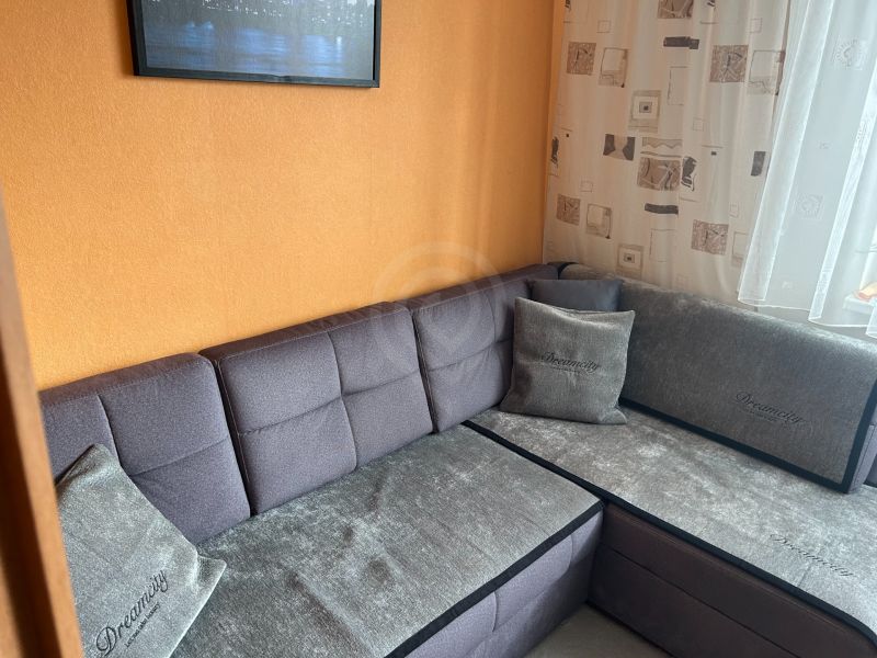 Gray sofa in the corner of the living room in a three-room apartment with an orange wall.