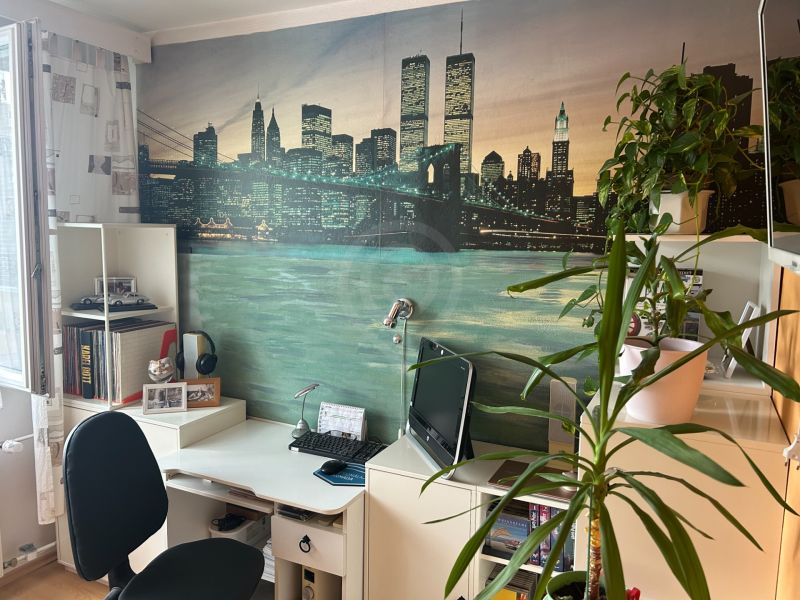 A workspace with a desk, plants, and decorative wallpaper in a 3-room apartment.