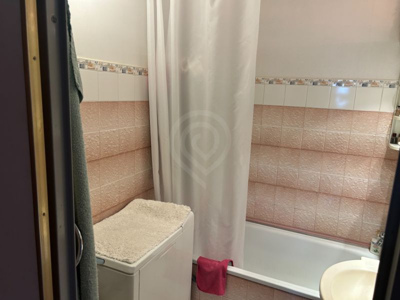 Bathroom with a bathtub, washing machine with a towel, and tiles in a 3-room apartment.