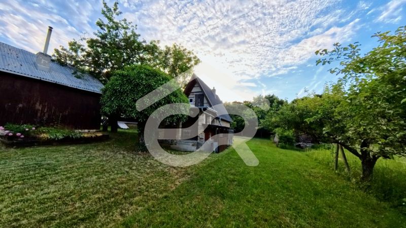 A cottage in Podhorany surrounded by greenery, with a blue sky and clouds in the background.