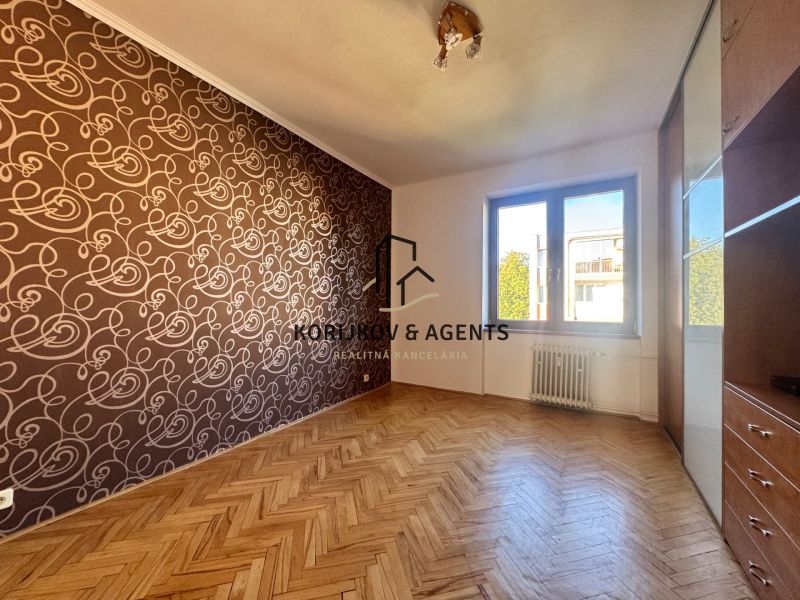 A room in a 4-room apartment with a wooden decor floor and patterned wallpaper.