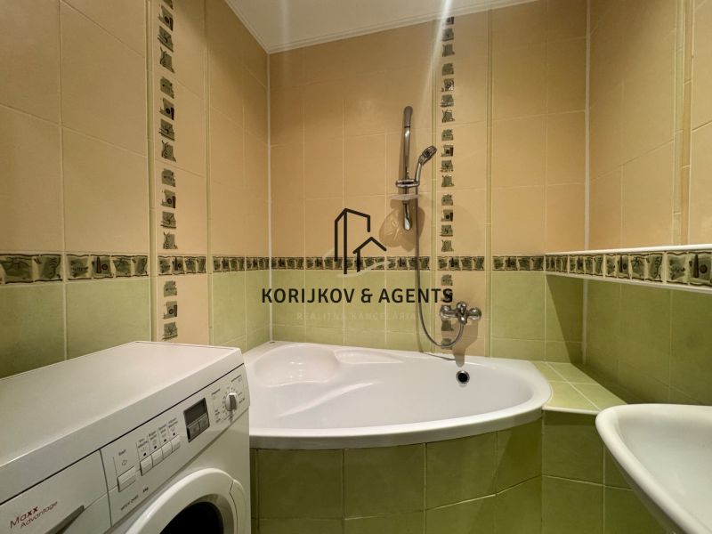 Bathroom in a 4-room apartment with a bathtub and a washing machine, green-cream tiles.