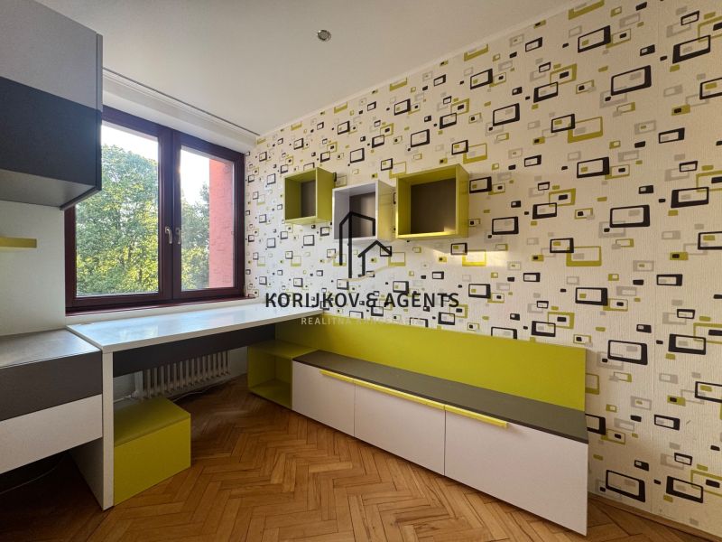 A room in a 4-room apartment with geometric wallpaper, furniture, and flooring with a wood decor.