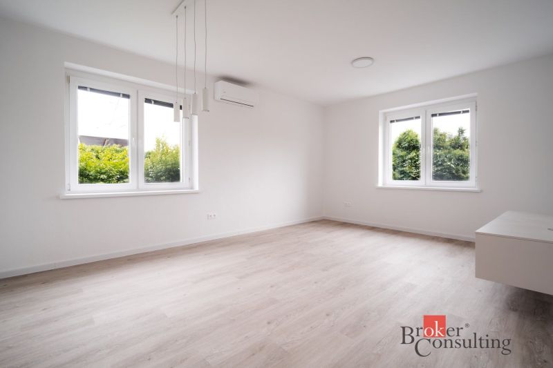 A bright room with wood-patterned flooring and large windows in a three-room apartment.
