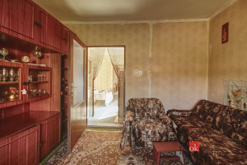 A room with a carpet, a sofa set, a glass cabinet, and a view into the adjacent room.