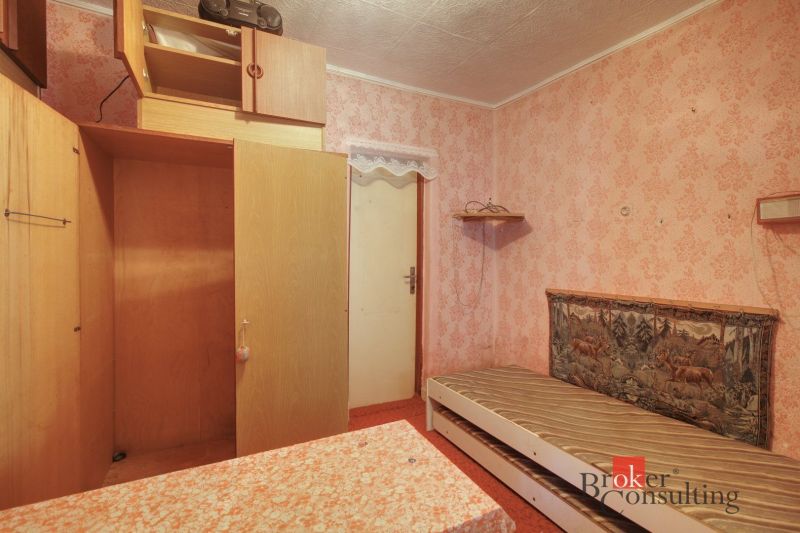 A room in a family house with a bed, a wardrobe, and pink wallpaper.