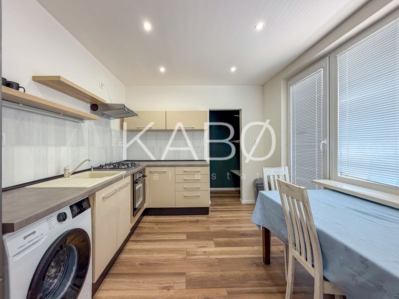 A kitchen in a 2-room apartment with appliances, a dining table, and a wooden decor floor.