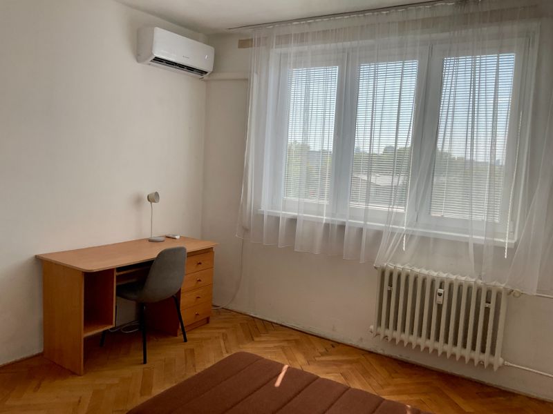 A room in a 2-room apartment with a desk, a chair, and air conditioning.