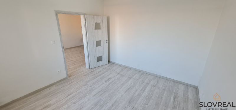 A room with a wooden decor floor and white doors in a 2-room apartment.