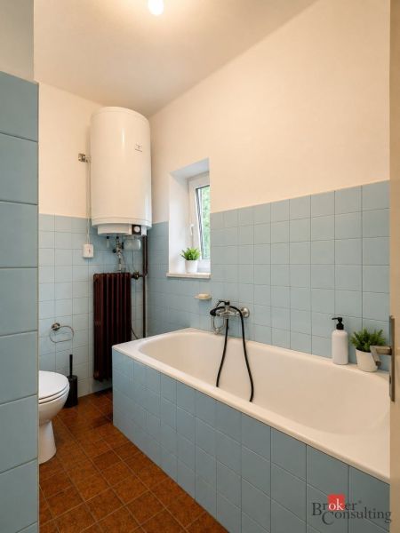 A bathroom in a family house with a bathtub, blue tiles, and a water heater on the wall.