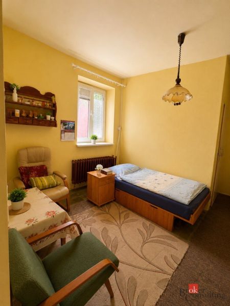 A room in a family house: bed, chairs, table, carpet, and window with blinds.