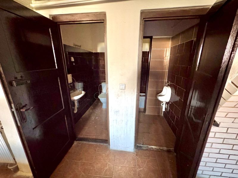 A bathroom in a family house with dark tiles and fixtures, divided into two rooms.