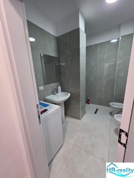 Bathroom in a 2-room apartment with a shower, washing machine, and ceramic tiles.