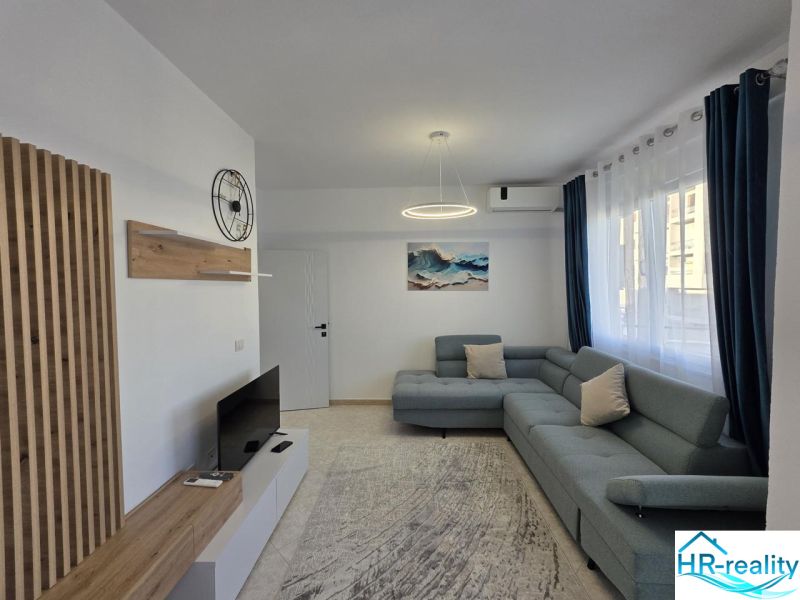 Living room in a two-room apartment with a sofa, television, and wooden decor.