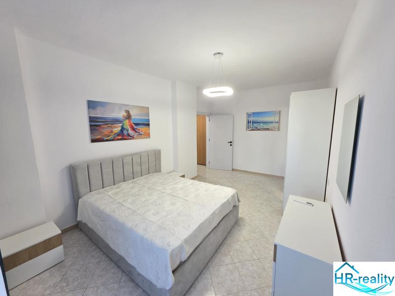 A bright bedroom in a two-room apartment with artistic paintings and white furniture.