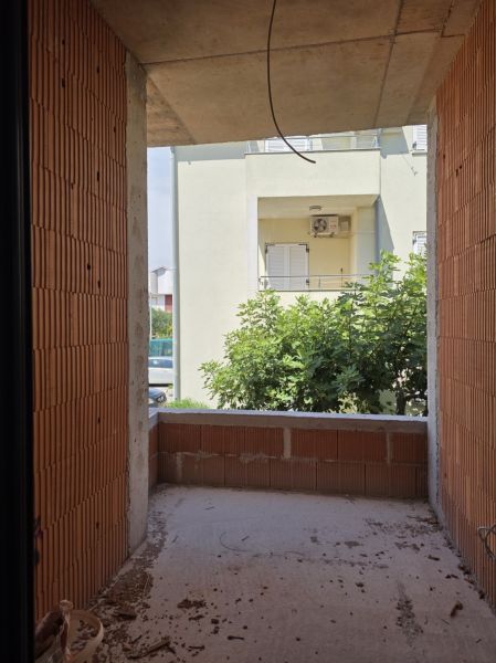 Unfinished balcony in a 3-room apartment with a view of greenery and the adjacent building.
