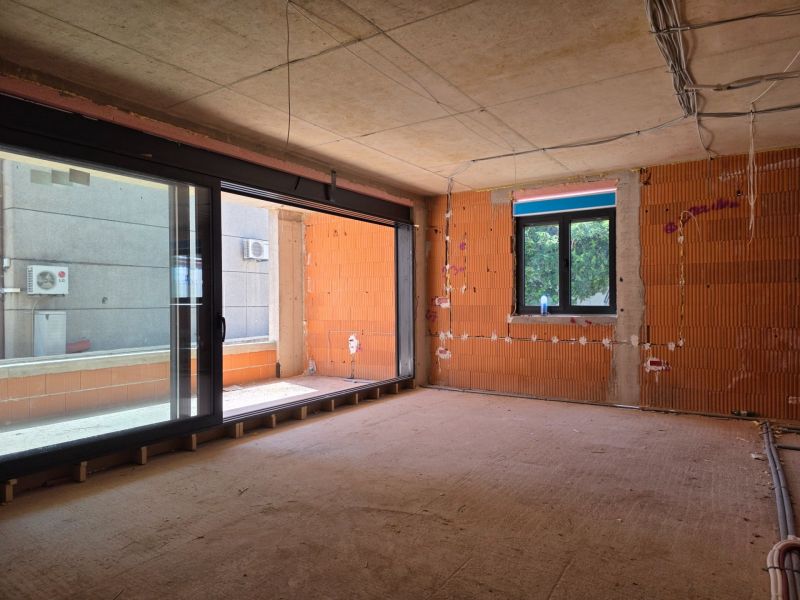 An unfinished 3-room apartment with large windows and exposed bricks without flooring.