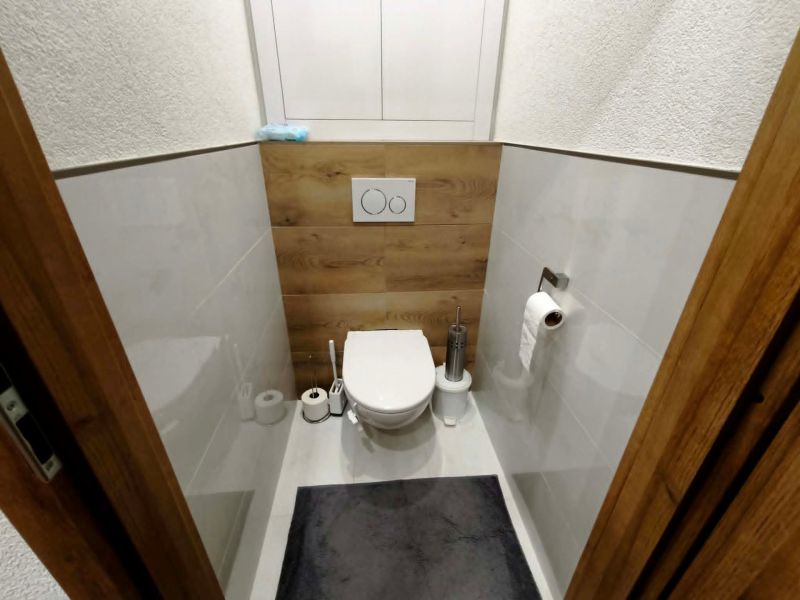 A toilet with a wooden floor decor and white tiles in a 3-room apartment.