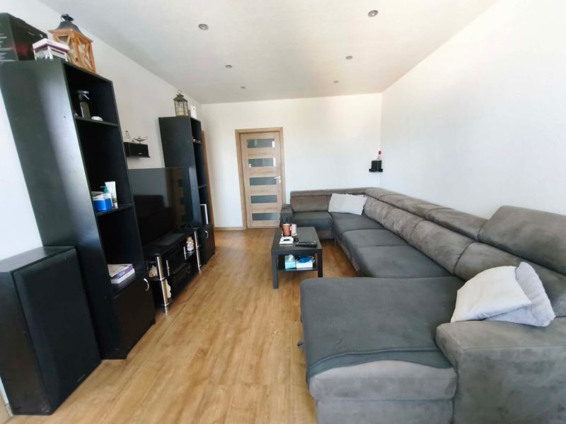 Living room with a large sofa, wooden decor flooring, and black furniture in a three-room apartment.