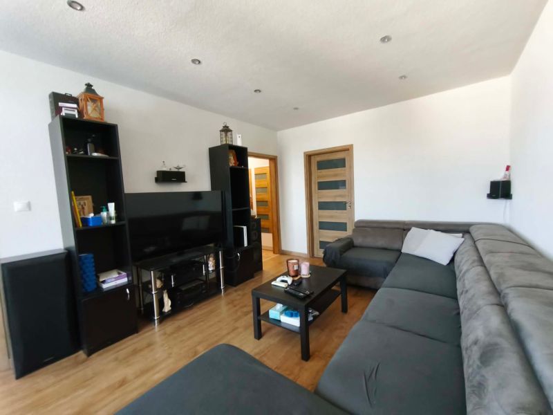 Living room in a 3-room apartment with a large sofa, television, and wooden decor flooring.