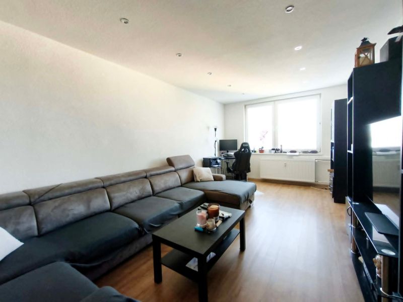 Living room in a 3-room apartment with a wooden decor floor, a sofa, and a PC desk.