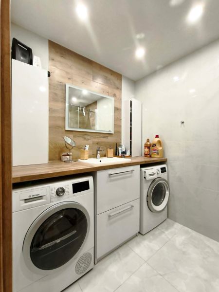 Bathroom in a 3-room apartment with a washing machine, dryer, and floor with wooden decor.