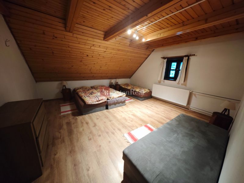 A room with three beds, a wooden decor floor, and a slanted wooden ceiling in a cottage.