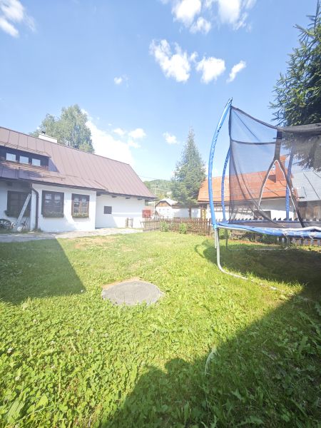A cottage in Špania Dolina with a trampoline on a grassy garden under a blue sky.