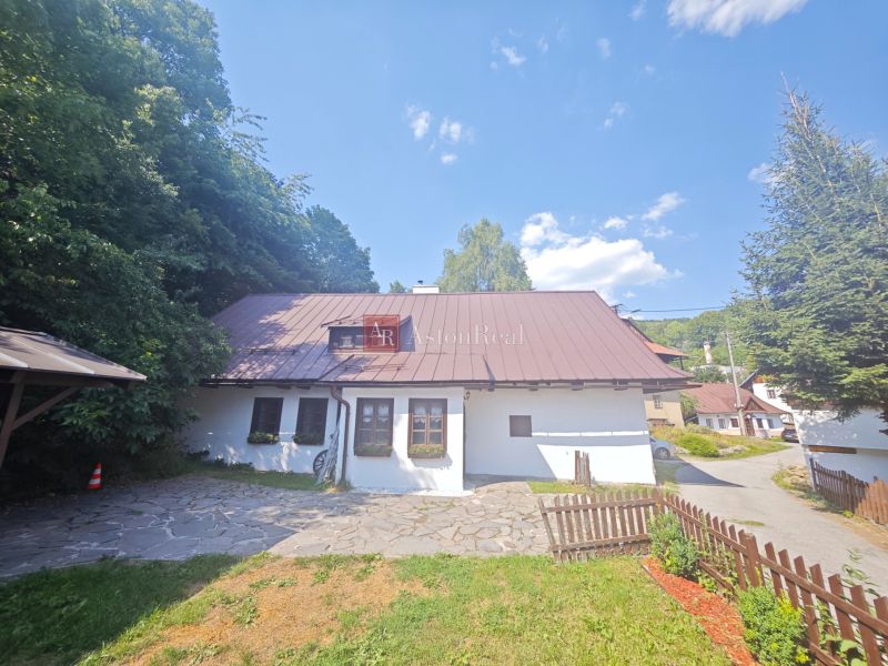 A cottage in Špania Dolina, surrounded by nature, with a stone path and a wooden fence.