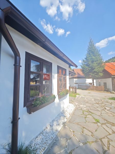 A cottage in Špania Dolina with a flower bed by the window and a paved walkway.