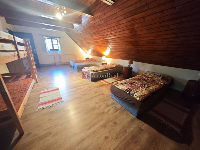 An attic room in a cottage with a wooden decor floor and multiple beds.