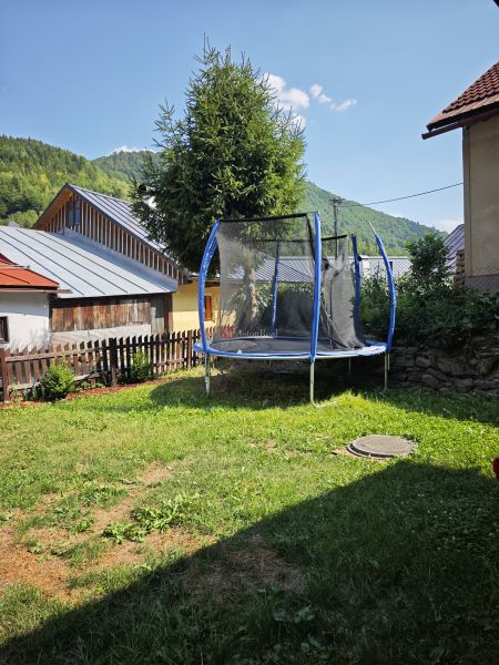 A trampoline near a cottage in Špania Dolina, surrounded by grass and trees in the background.