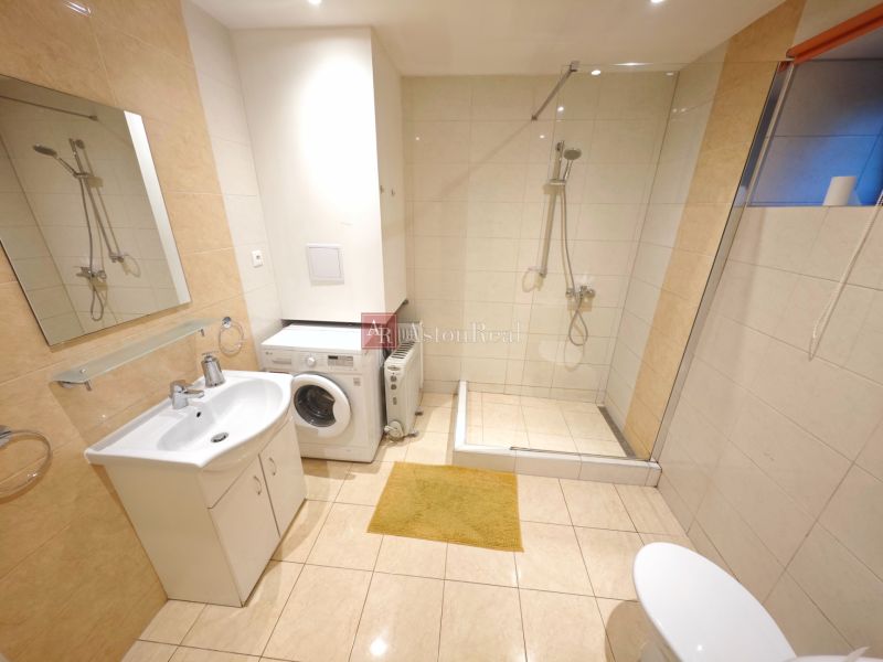 A bathroom in a cabin with a washing machine, shower stall, and floor with wooden decor.