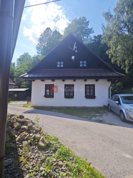 A cottage in Špania Dolina with a white facade and a satellite dish, surrounded by greenery.