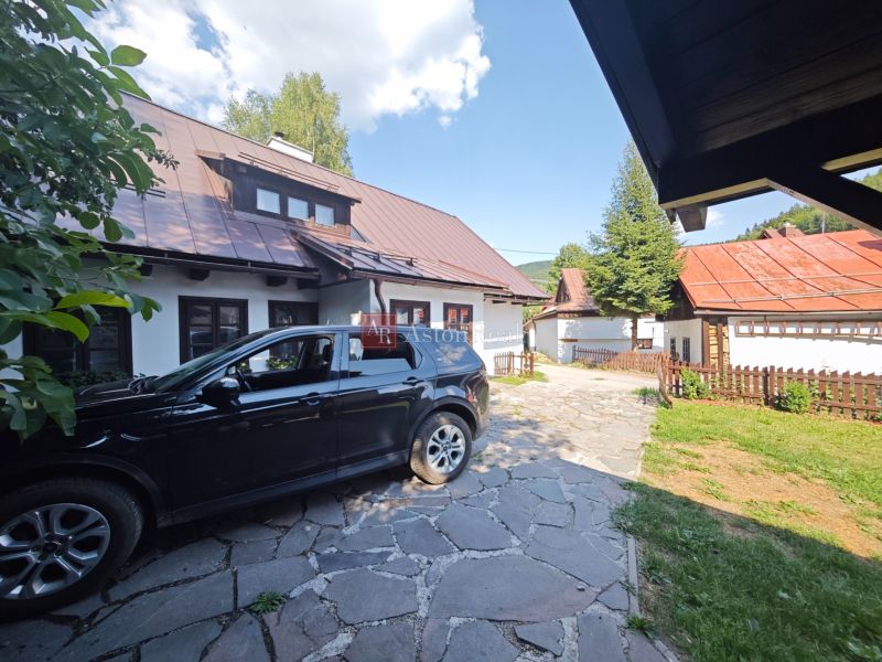 A car parked near a cottage in Špania Dolina, with visible roofs and a fence.
