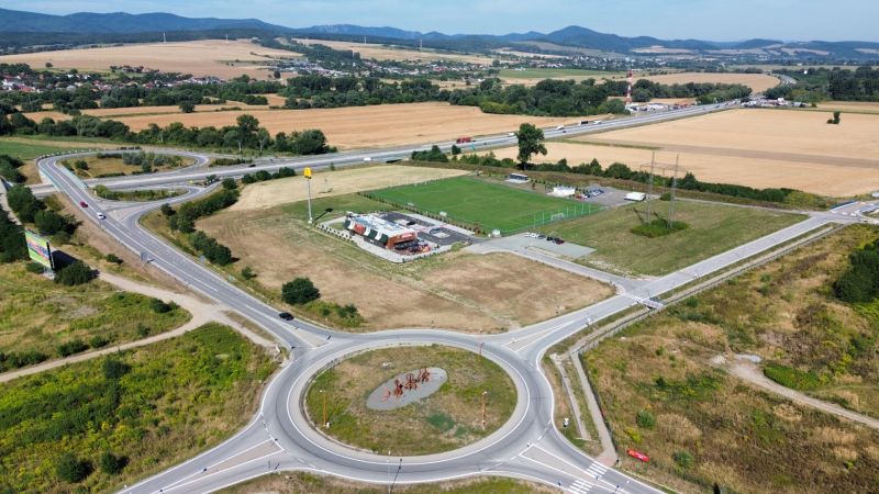 Roundabout and highway in Nová Polhora surrounded by fields and a sports field.