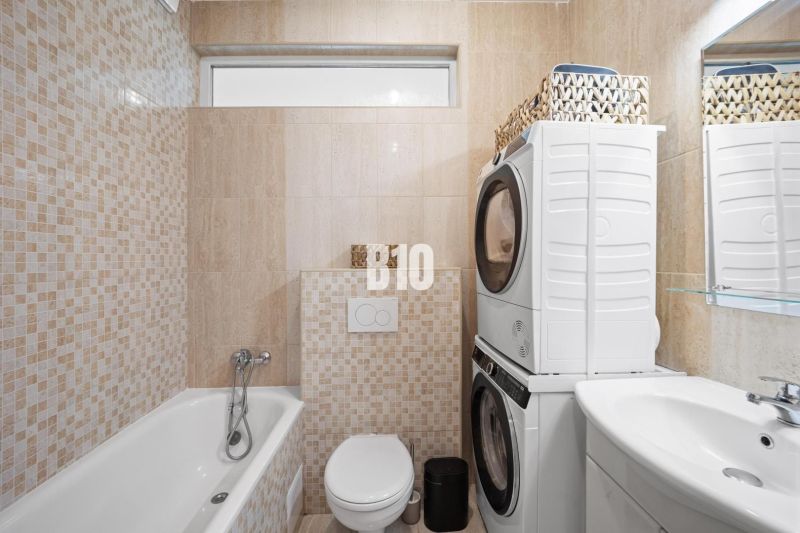 Bathroom in a 2-room apartment with a washing machine, dryer, bathtub, and toilet.