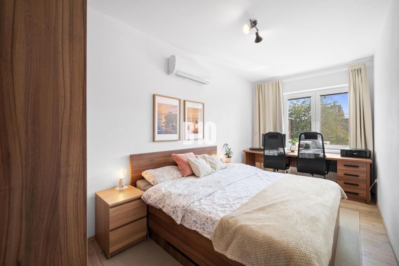 Bedroom in a 2-room apartment with wood-patterned flooring and a desk.