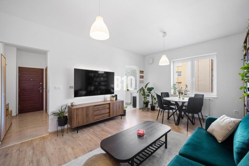 A bright living room of a two-room apartment with a wooden decor floor and a dining table.