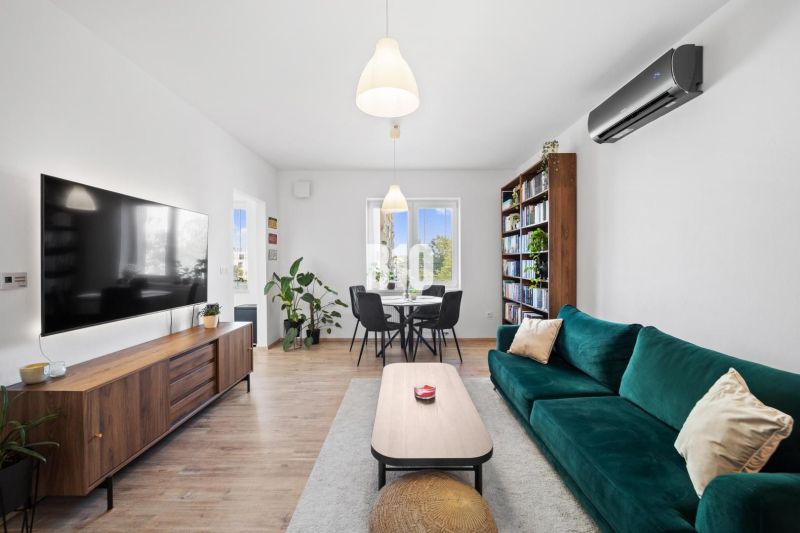 Living room in a two-room apartment with a large television, a bookshelf, and a wooden decor floor.