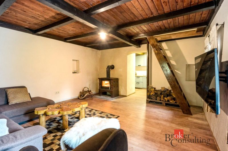 The interior of a cottage with a wooden beam ceiling, a stove, and a floor with a wooden decor.
