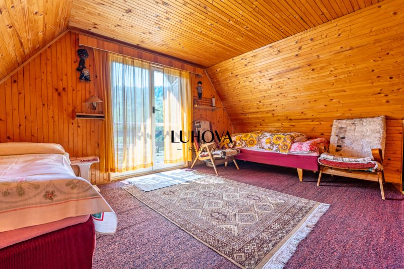 A room in a cabin with wooden paneling, a bed, an armchair, and a carpet on the floor.